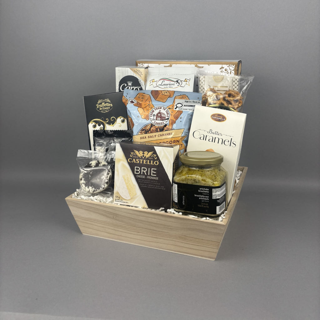 A wooden gift basket filled with assorted gourmet snacks, crackers, a jar of artichoke bruschetta spread, and packaged sweets.