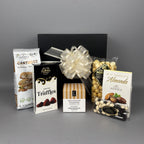 A chocolate and snack gift box featuring a black gift box tied with a large cream ribbon, surrounded by assorted packaged treats including Cantucci cookies, truffles, caramel popcorn, milk chocolate almonds, and white & dark chocolate raisins.