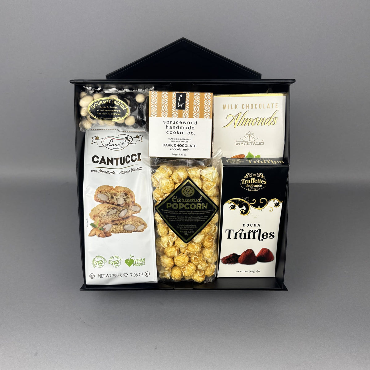 A gourmet chocolate and snack gift basket presented in a black container. The basket contains a bag of Cantucci almond biscotti, Sprucewood Handmade Cookies, caramel popcorn, and other assorted sweets. 