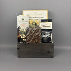 A gourmet chocolate and snack gift basket arranged in a dark rustic wooden box. The basket contains assorted packaged snacks including milk chocolate bar, caramel popcorn, milk chocolate almonds, milk chocolate shortbread, and gourmet frolletti cookies.