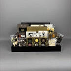 A chocolate gift basket display on a black serving tray, featuring assorted chocolates, truffles, packaged sweets, and brands including Made, Cookie It Up, Hamlet, Lexus, and more.
