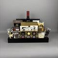 A luxury chocolate and wine gift basket arranged in a black wooden tray. The basket includes a bottle of red wine, assorted gourmet chocolates, truffles, shortbread cookies, and packaged sweets from brands like Made Chocolate and Hamlet.