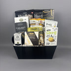 A gourmet gift basket filled with assorted packaged snacks, cheeses, crackers, and artichoke bruschetta, arranged in a black rectangular basket.
