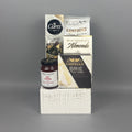 A curated gourmet gift hamper featuring Castello Brie cheese, a box of milk chocolate Almonds, a bag of Cantucci almond biscotti, and a box of Carr's crackers, all arranged on a white rustic wood box.