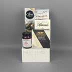 A curated gourmet gift hamper featuring Castello Brie cheese, a box of milk chocolate Almonds, a bag of Cantucci almond biscotti, and a box of Carr's crackers, all arranged on a white rustic wood box.