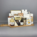 A gourmet gift hamper arranged on a wooden serving board. The assortment includes artisanal cheeses, crackers, nuts, a bottle of fresh lime vinegar, and packaged snacks from brands such as Provisions, Castello Brie, and Belberry.
