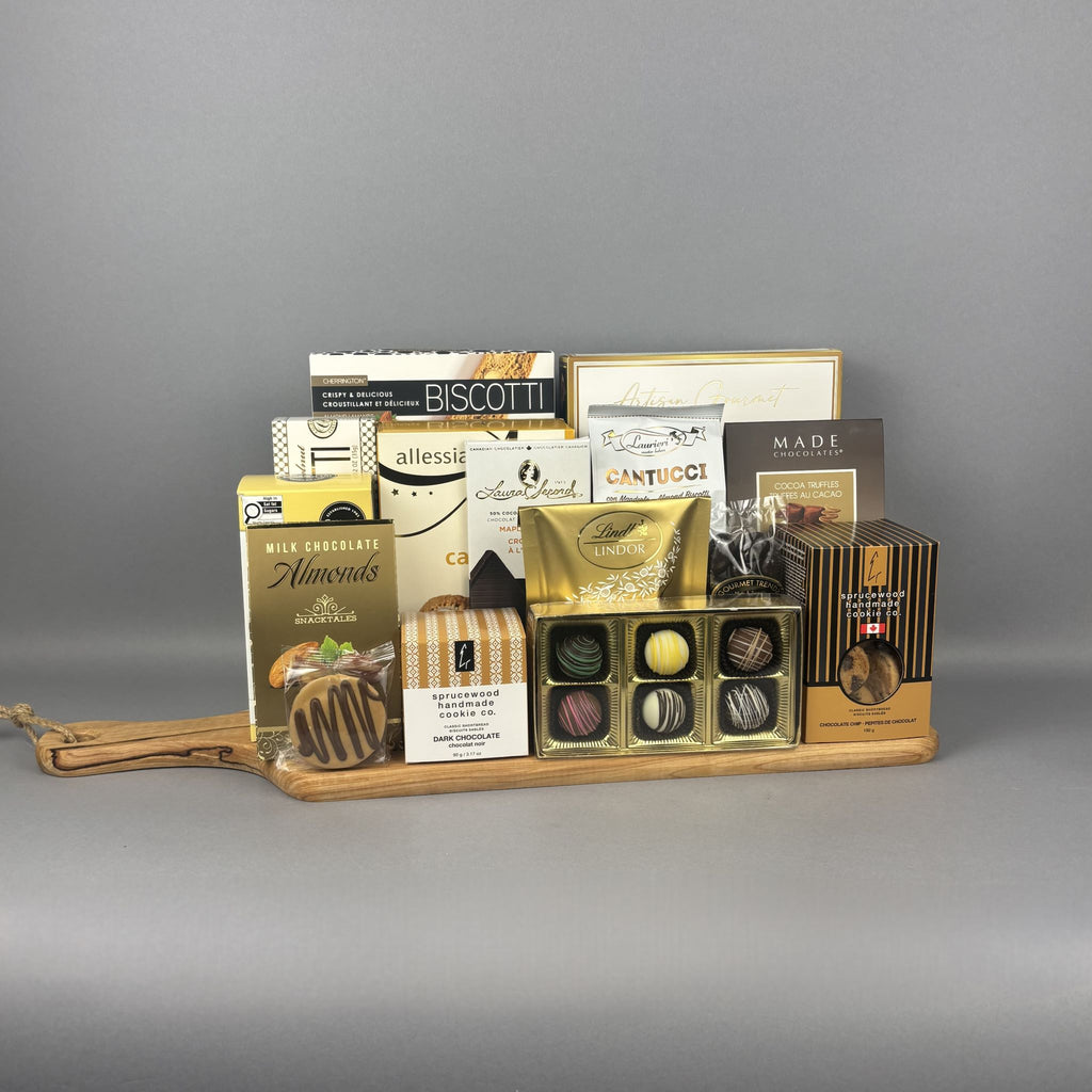 A gourmet chocolate and snack gift board arranged on a wooden serving tray. The assortment includes boxes of Biscotti, Allessia cookies, Lindt Lindor chocolates, and other sweet treats in elegant packaging.