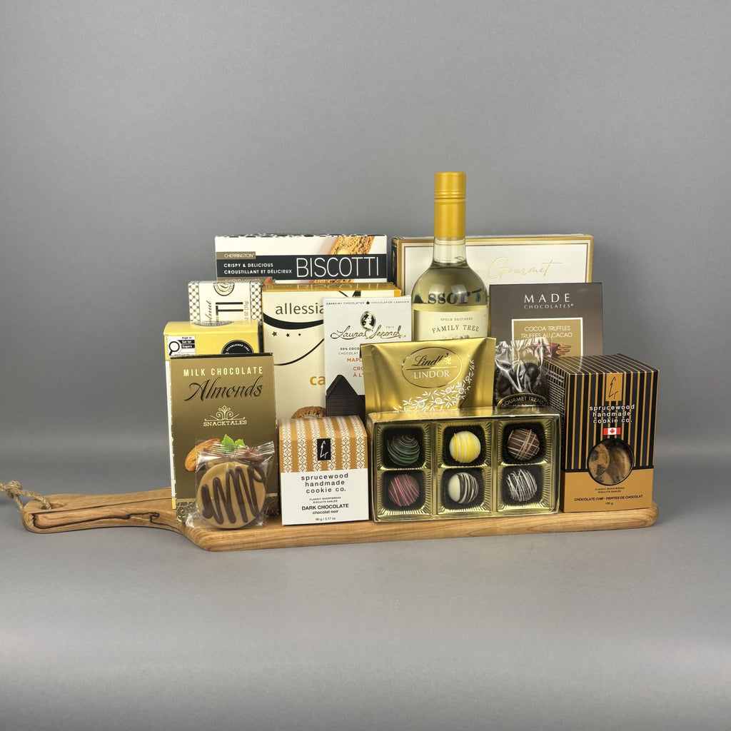 A gourmet gift hamper arranged on a wooden tray, featuring a bottle of white wine, assorted chocolates, biscuits, and packaged treats.