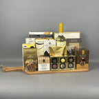 A gourmet gift hamper arranged on a wooden tray, featuring a bottle of white wine, assorted chocolates, biscuits, and packaged treats.