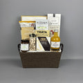 A gourmet gift basket arranged in a brown fabric basket with black handles, filled with assorted food items including a bottle of vinegar, pistachios, brie cheese, salmon pocket, and breadsticks.