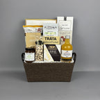 A gourmet gift basket arranged in a brown fabric basket with black handles, filled with assorted food items including a bottle of vinegar, pistachios, brie cheese, salmon pocket, and breadsticks.