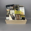 A gourmet gift hamper arranged in a light wood tray, containing packaged snacks and foods including Hardbite chips, breadsticks, Tràta Tuna Pocket, Castello Brie, and a jar of Provisions jam.
