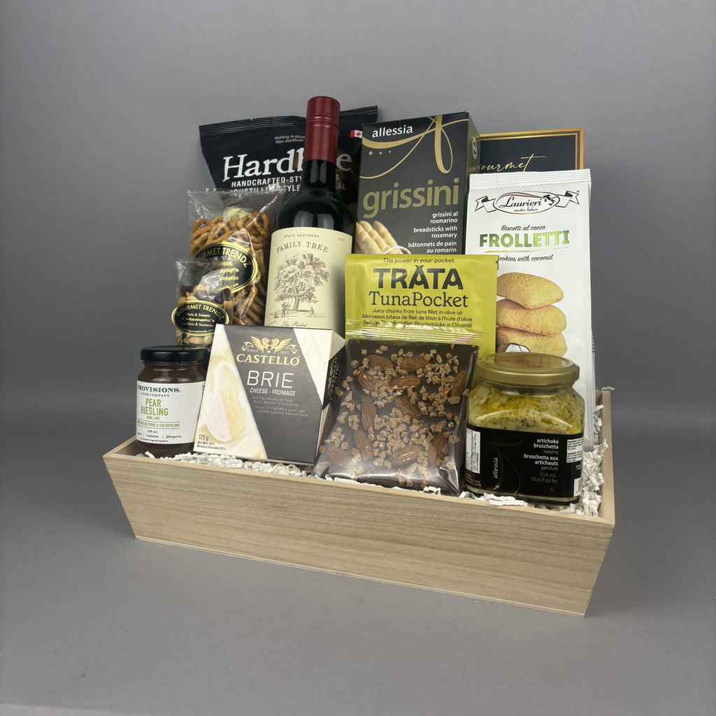 A gourmet gift hamper in a light wood box filled with assorted Italian snacks, crackers, a bottle of red wine, and packaged foods.