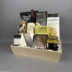A gourmet gift hamper in a light wood box filled with assorted Italian snacks, crackers, a bottle of red wine, and packaged foods.