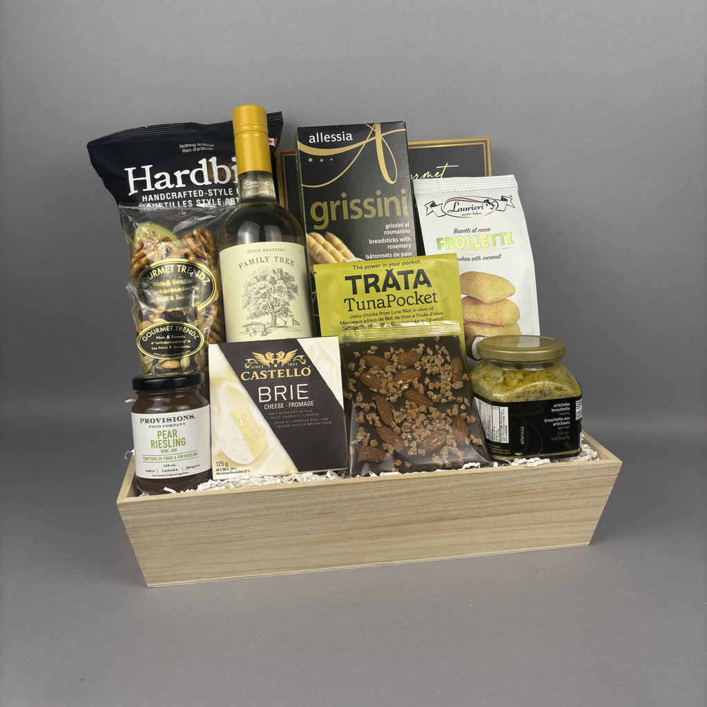 A wooden gift basket filled with assorted gourmet snacks, a bottle of white wine, and packaged food items.
