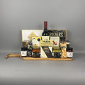 A gourmet gift hamper arranged on a wooden tray. The hamper includes a bottle of Family Tree Wine, option of Caberent-Merlot or Sauvignon Blanc, Smoked Salmon Pocket, a box of Castello Brie cheese, a box of Crackers, jars of preserves, nuts, and other gourmet items.