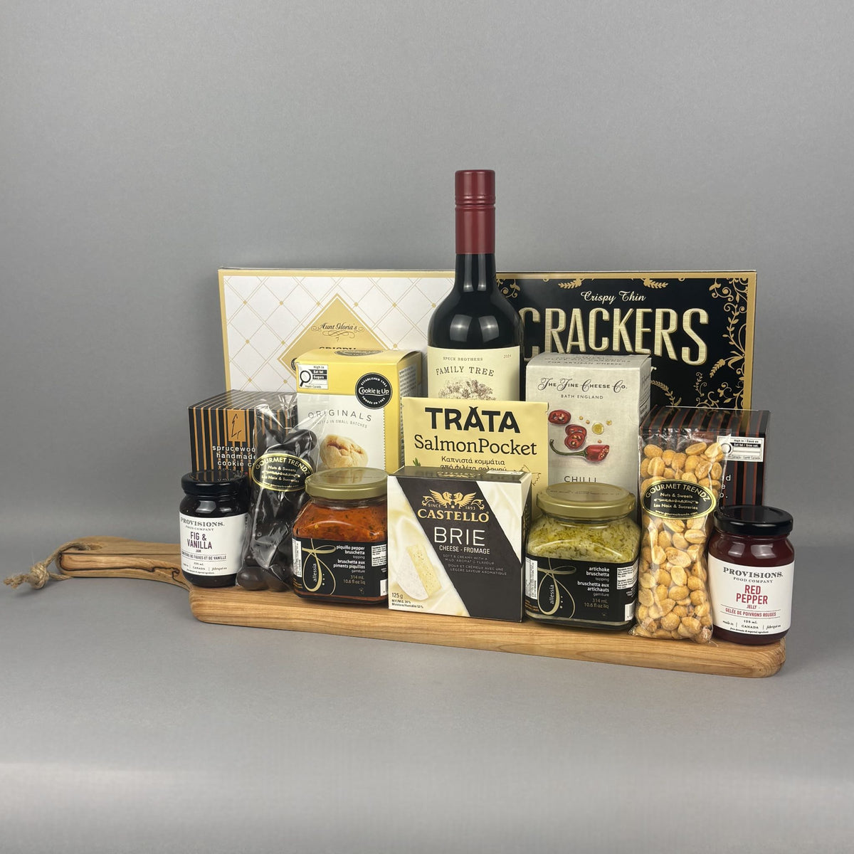 A gourmet hamper gift set arranged on a wooden tray. The set includes a bottle of wine, a box of crackers, brie cheese, smoked salmon pocket, spreads, jars, and nuts.
