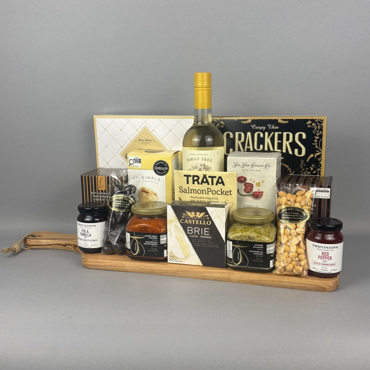 A gourmet gift hamper arranged on a wooden tray. The hamper includes a bottle of Tráta Smoked Salmon, Castello Brie cheese, a box of crackers, jars of spreads, and bags of nuts.