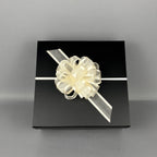 A square black gift box wrapped with a white ribbon and a large cream-colored decorative bow.