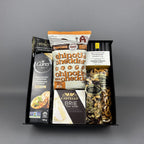 A curated snack and cheese gift basket arranged in a black box, featuring Carr's crackers, Castello Brie cheese, a bag of chipotle cheddar popcorn, and a bag of mixed nuts.