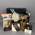 A gourmet gift hamper showcasing the black presentation box with a white ribbon, assorted snacks including popcorn, brie cheese, pretzels, and biscuits.