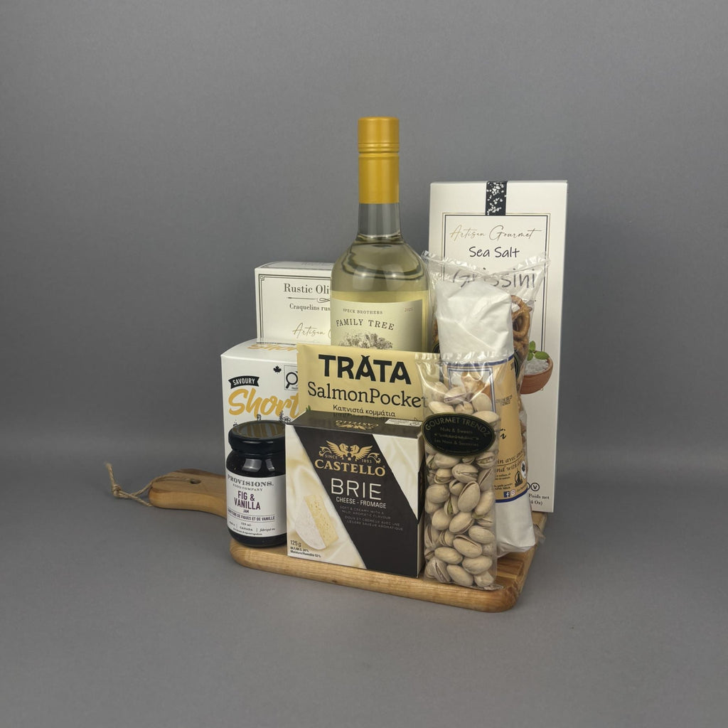 A gourmet gift hamper arranged on a small wooden tray. The set includes a bottle of white wine, Tráta Smoked Salmon, Castello Brie cheese, Canadian Cheddar Biscuits , Sea Salt breadstick, pistachios, and a dried salami stick.