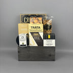 A gourmet gift hamper arranged in a dark wooden box. The hamper contains a box of artichoke bruschetta, a salmon pocket, a bag of gourmet pretzels, a Canadian Cheddar biscuits, and a box of crispy crackers.