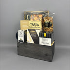 A gourmet gift hamper in a dark wood crate, featuring Castello Brie cheese, Tráta Salmon Pocket, pretzels, and other savoury snacks.