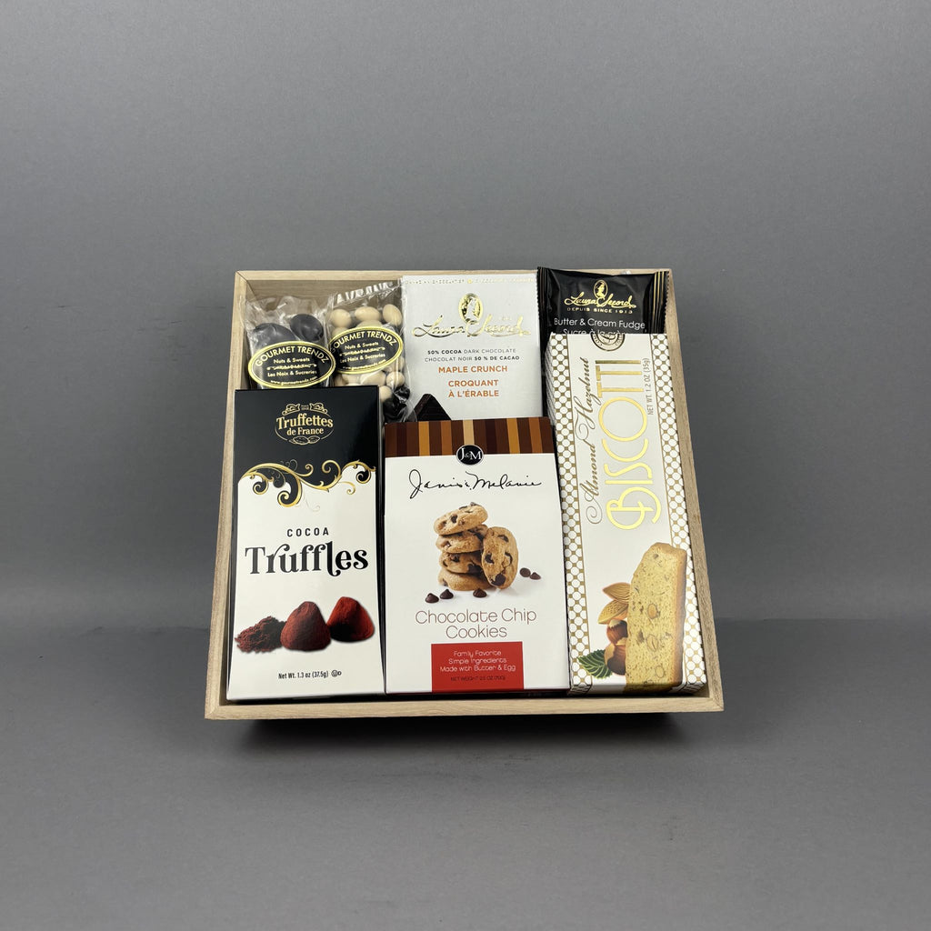 A gourmet chocolate and cookie gift box set in a light wood tray, featuring various branded packaged sweets including, J&M chocolate chip cookies, Laura Secord chocolate bar and butter and cream fudge, dark chocolate almonds, and chocolate covered raisins. 