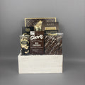 A chocolate gift basket arranged in a white wooden crate. The basket contains a box of Cookie It Up Milk Chocolate shortbread cookies, a box of Made Chocolate Toffee truffles, Chocolate Almonds, and a handcrafted bark bar.