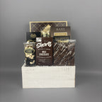 A chocolate gift basket arranged in a white wooden crate. The basket contains a box of Cookie It Up Milk Chocolate shortbread cookies, a box of Made Chocolate Toffee truffles, Chocolate Almonds, and a handcrafted bark bar.