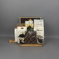 A chocolate gift basket arranged on a wooden tray. The basket contains assorted chocolates, including a bag of Cantucci, milk chocolate almonds, a bag of chocolate-covered raisins , and other packaged sweets.