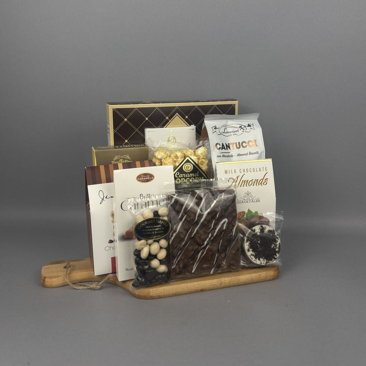 A gourmet chocolate and snack gift basket arranged on a small wooden tray. The basket includes packaged chocolates, almonds, candies, and a sugar cookie box.