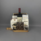 A gourmet gift hamper featuring a bottle of red wine, assorted chocolates, caramel candies, and almond chocolate on a wooden tray.