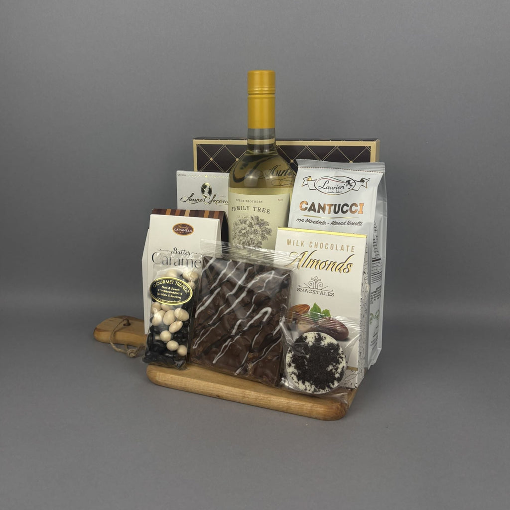 A gourmet gift hamper featuring a bottle of white wine, assorted chocolates, almonds, and other snacks arranged on a wooden tray.