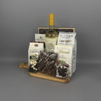 A gourmet gift hamper featuring a bottle of white wine, assorted chocolates, almonds, and other snacks arranged on a wooden tray.