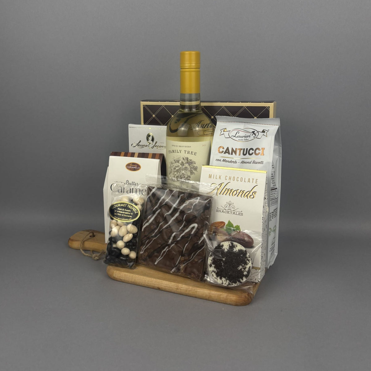A gourmet gift hamper featuring a bottle of white wine, assorted chocolates, almonds, and other snacks arranged on a wooden tray.
