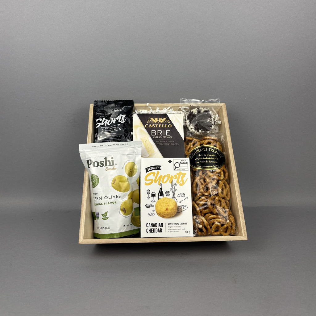 A curated snack gift box arranged in a light wood tray, featuring Poshi Green Olives, Castello Brie cheese, and Short's Canadian Cheddar crackers.
