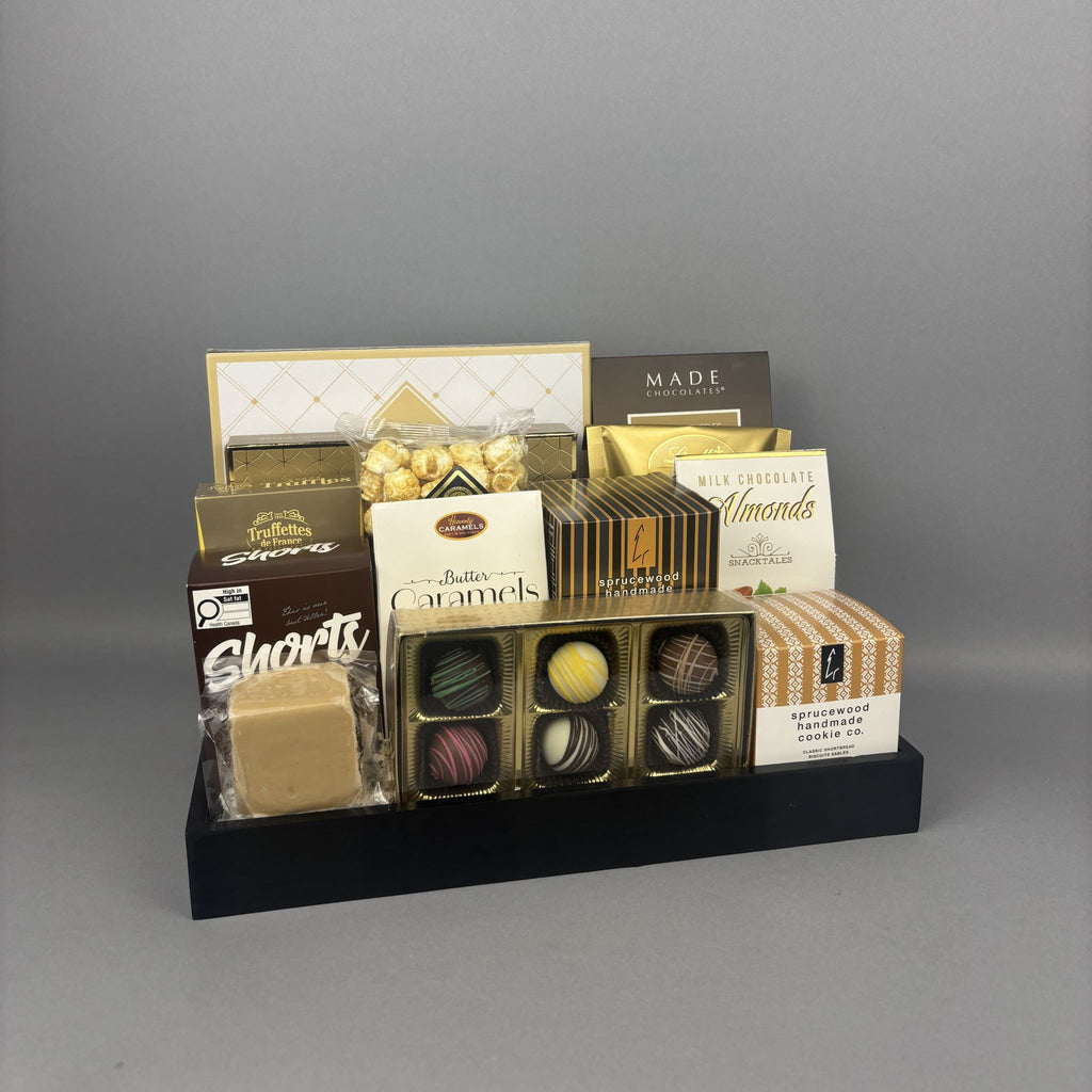 A chocolate and almond gift basket arranged on a black rectangular tray. The set includes an assortment of handcrafted truffle chocolates, chocolate almonds, a bar maple fudge, and several other assorted sweets.