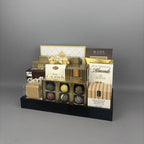 A gourmet chocolate and almond gift basket arranged on a black tray. The assortment includes various boxed chocolates, pralines, almonds, and a bag of cookies, with several brands including Lindt, Sprucewood, Mad Chocolates, Aunt Gloria's and more.