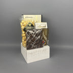 A gift basket arrangement of snacks and chocolates displayed on a white wooden basket. The assortment includes Allessia biscotti, a box of chocolate-covered almonds, and a box of Lindt chocolate truffles.