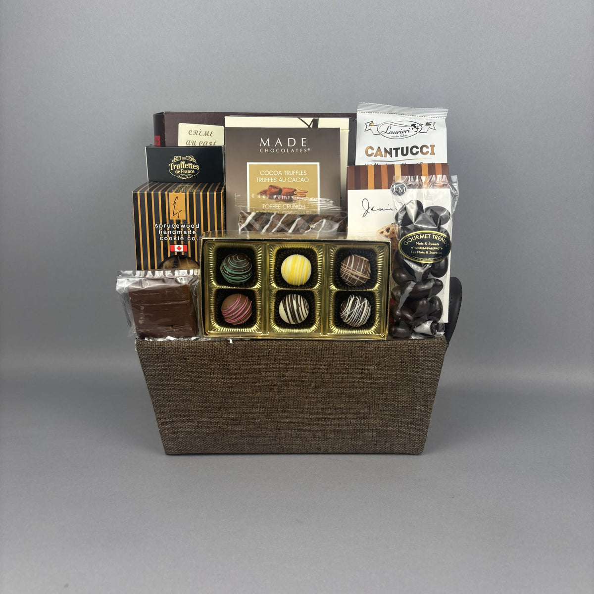 A gourmet chocolate gift basket in a brown woven basket, filled with assorted chocolates, truffles, and chocolate bars from brands like Made and Sprucewood.