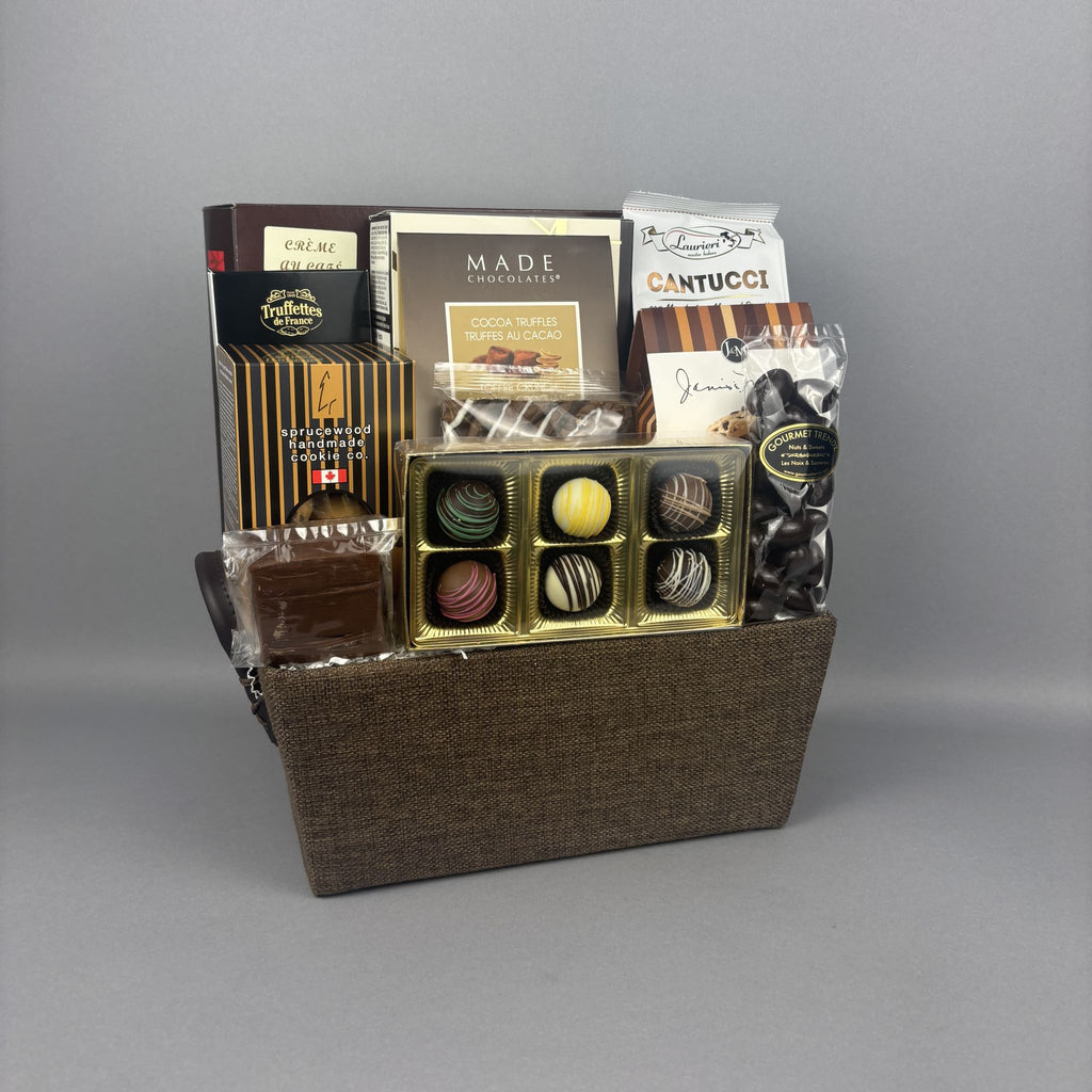 A gourmet chocolate gift basket in a brown woven basket, filled with assorted chocolates, truffles, and boxed sweets including brands like Made and Lexus.