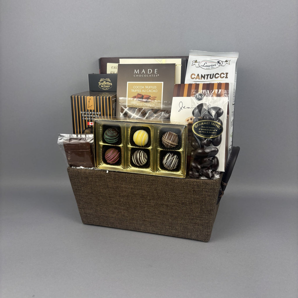 A gourmet chocolate gift basket in a brown woven basket, filled with assorted chocolates, truffles, and chocolate bars including Old English Fudge and Made Chocolates.